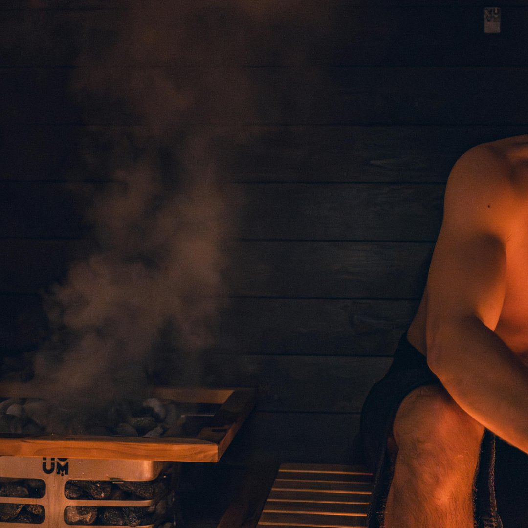 Person sitting in a sauna with steam rising from a wooden bench.